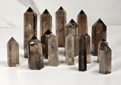 A group of smoky quartz crystal points of various sizes arranged on a white surface with a light gray marble-patterned background.