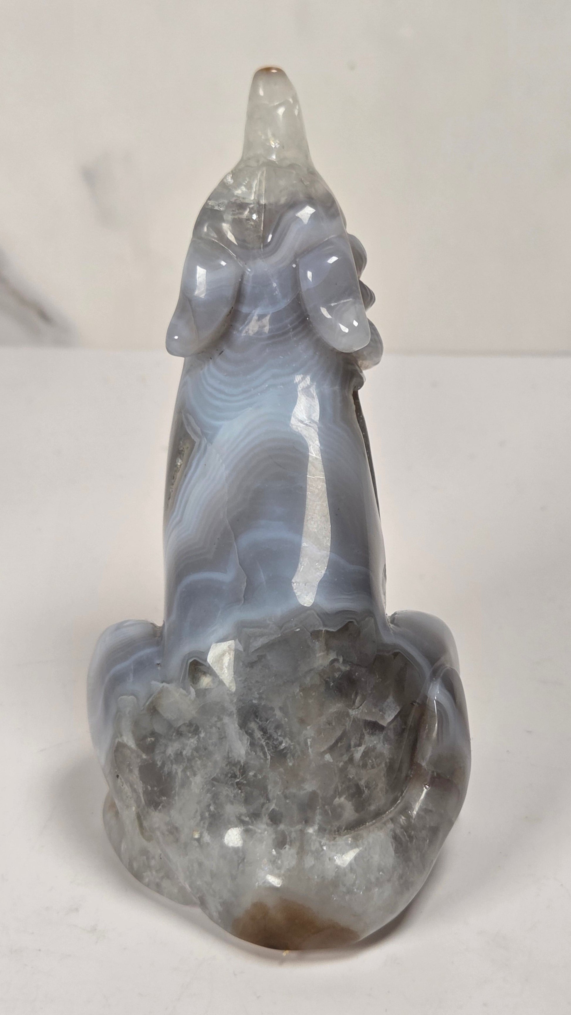 A polished agate figurine sculpted in the shape of a deer, featuring natural banding patterns in shades of gray, blue, and white, set against a light marble background.