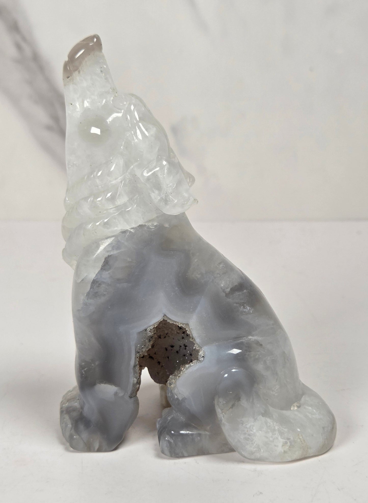 A carved stone dog figurine in a sitting position, made from a semi-translucent gray and white agate-like material with natural speckling, set against a light neutral background.