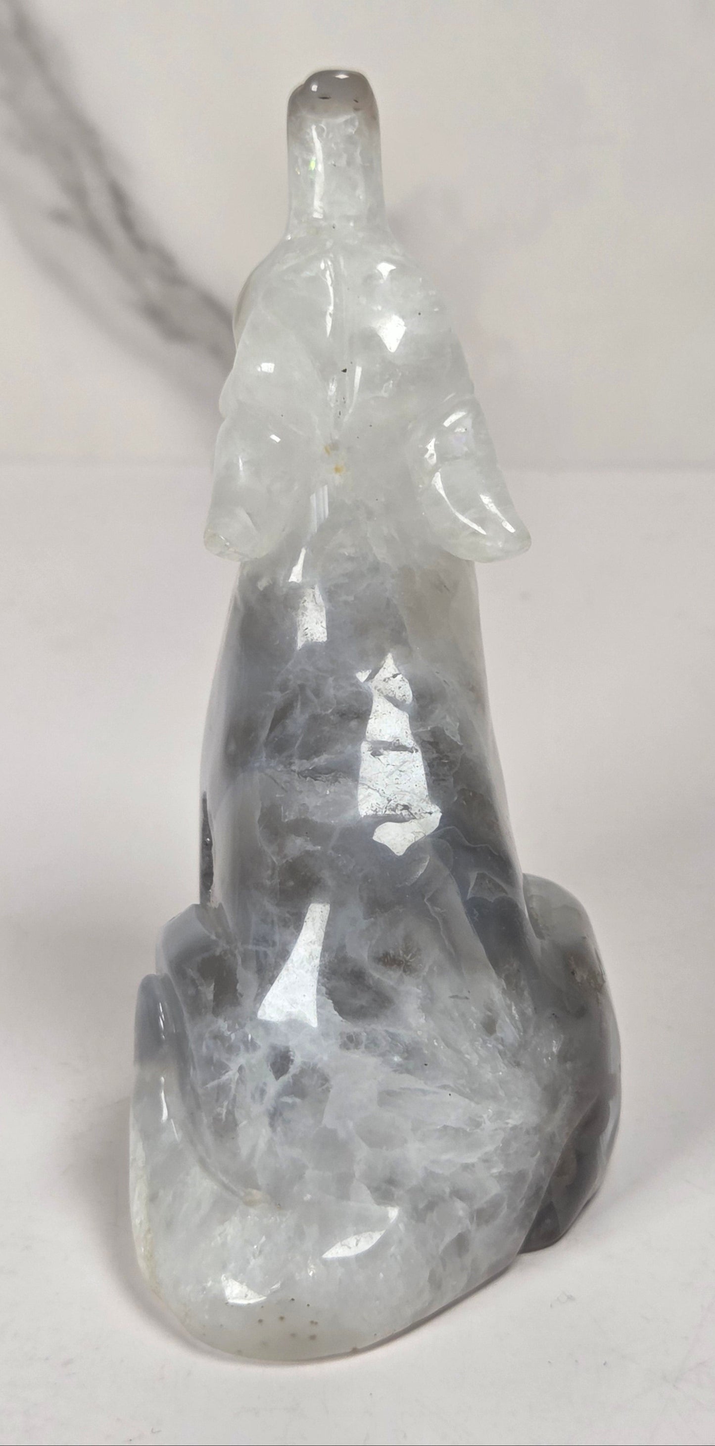 A carved crystal figurine of a seated figure, made from gray and white marbled stone, photographed against a light gray marble-patterned background.
