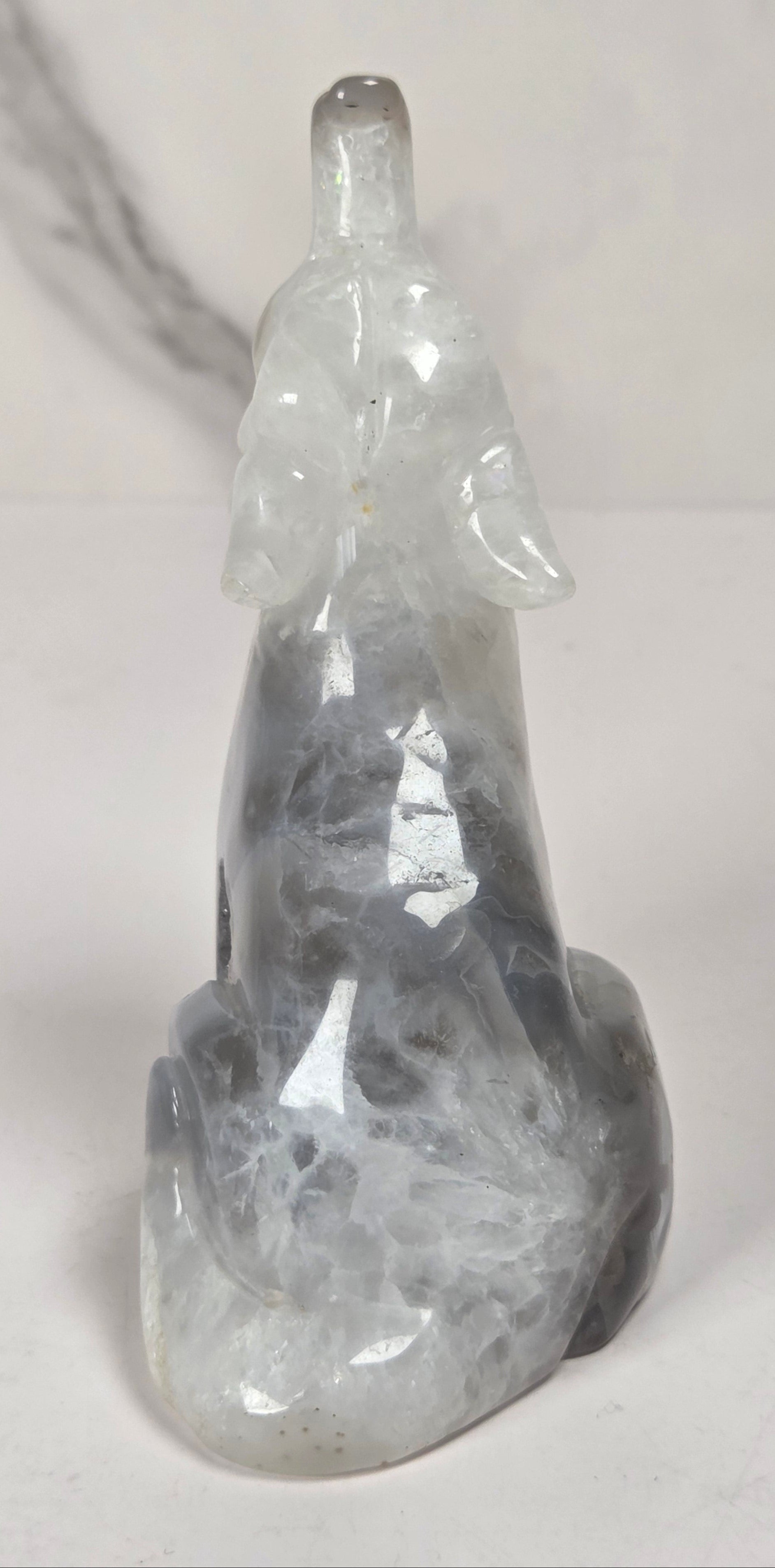 A carved crystal figurine of a seated figure, made from gray and white marbled stone, photographed against a light gray marble-patterned background.