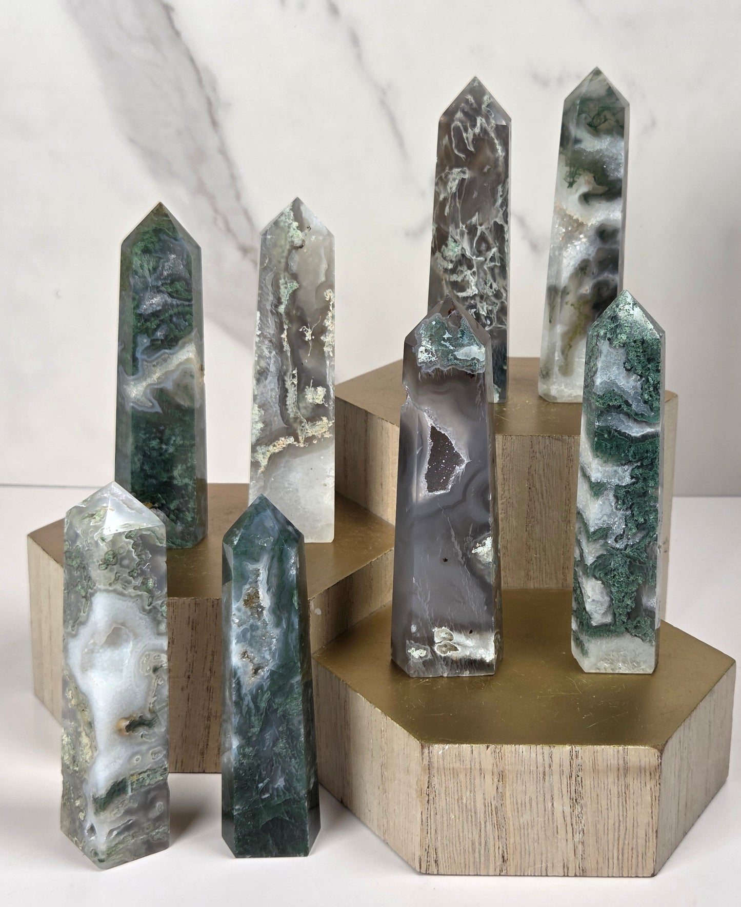 A set of polished natural crystal points in various colors and patterns, displayed on light wood blocks with a gold-colored hexagonal base against a white marble background.