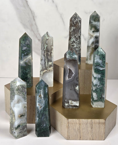 A set of polished natural crystal points in various colors and patterns, displayed on light wood blocks with a gold-colored hexagonal base against a white marble background.
