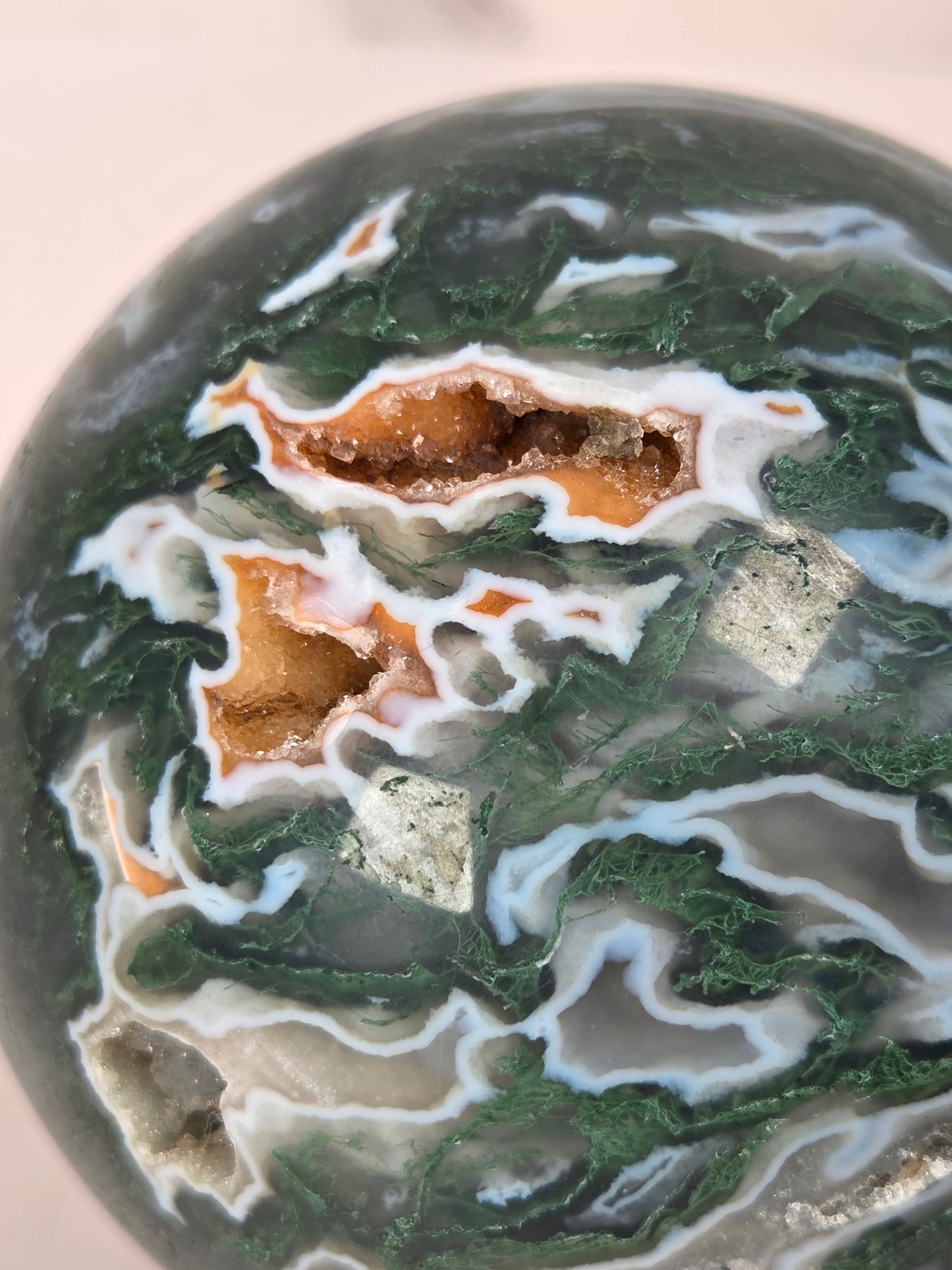 A polished agate crystal sphere with swirling green, gray, and black bands, displayed on a clear acrylic stand next to a wooden letter tile spelling 'A1' on a light marble surface.