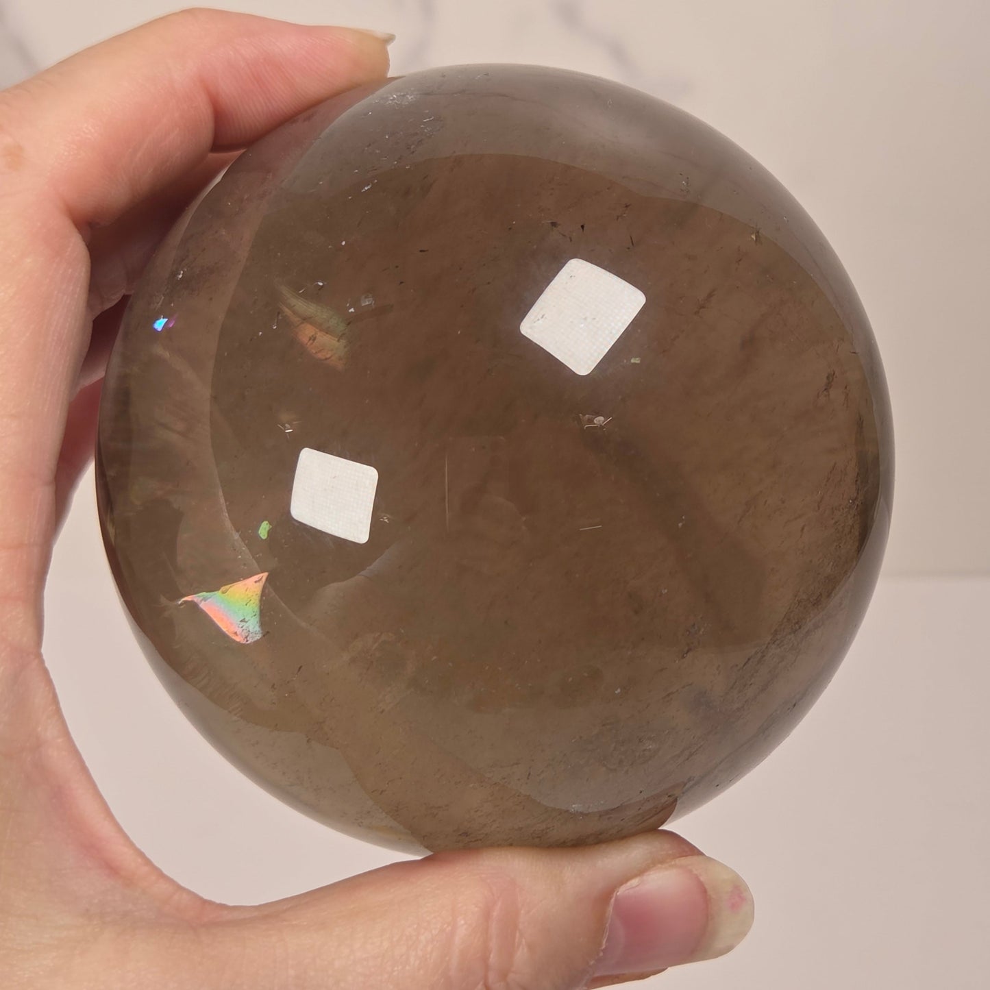A hand holding a large, smooth, polished brown smoky stone sphere against a light neutral background.