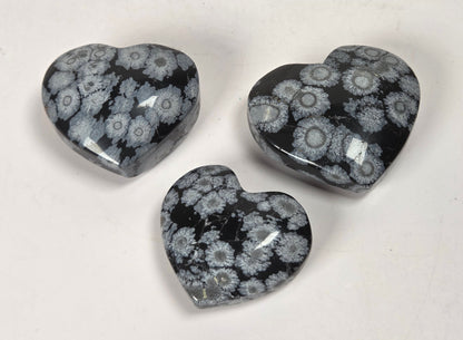 Three heart-shaped polished gemstone pendants featuring a black and gray floral or coral-like pattern, arranged on a plain off-white background.