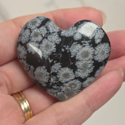 A heart-shaped polished stone with a black and white coral-like pattern, held in a person's hand.