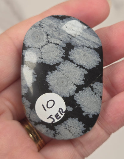 A hand holding a polished black stone with a white and gray marbled pattern, featuring a small white circular sticker that reads '10 JER'.