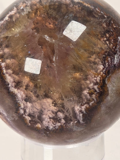 A polished brown crystal sphere with pinkish-purple and amber inclusions, displayed on a clear stand against a light background.