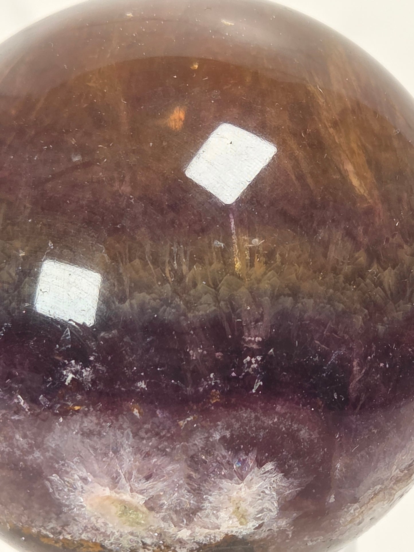 A close-up of a polished oval gemstone with a gradient of deep purple and brown, showing natural crystalline textures and internal inclusions.