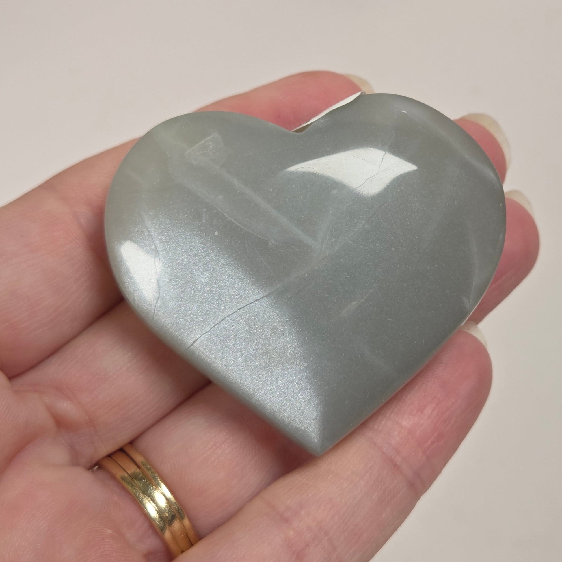 A heart-shaped gray stone or crystal held in a person's hand against a light marble-patterned background.
