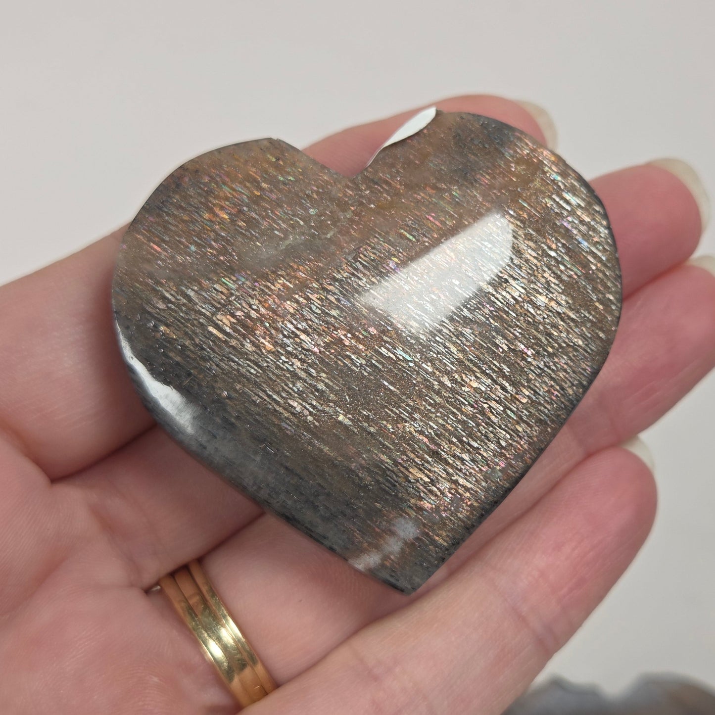 A heart-shaped polished stone with a metallic copper and silver glitter finish, held in a person's hand. A second similar stone is blurred in the background.