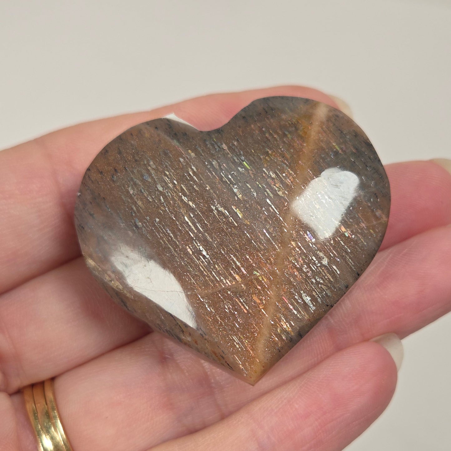 A heart-shaped polished stone with a brown and gold mottled pattern, held in a person's hand. The stone has white patches on its top surface and is photographed against a light gray background.