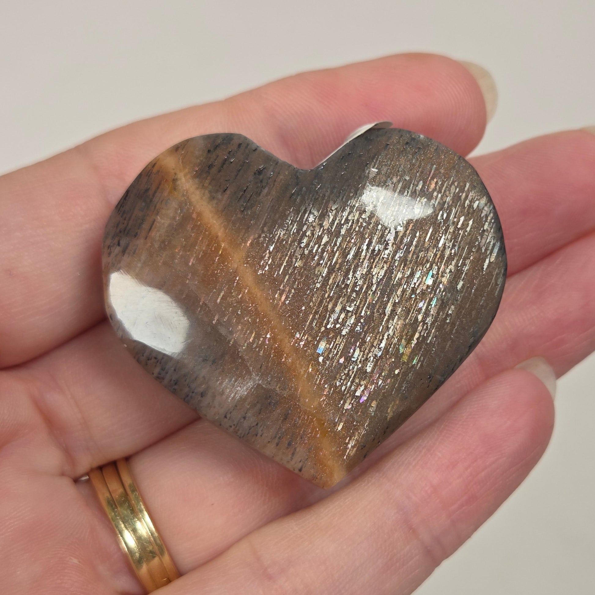 A heart-shaped polished stone with a brown and black marbled pattern and a diagonal golden-brown band, held in a person's hand.