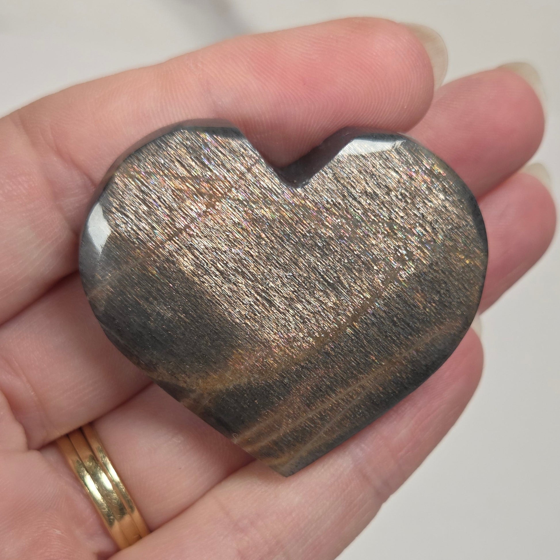 A heart-shaped polished stone with a metallic gold and dark gray banded pattern, held in a person's hand.