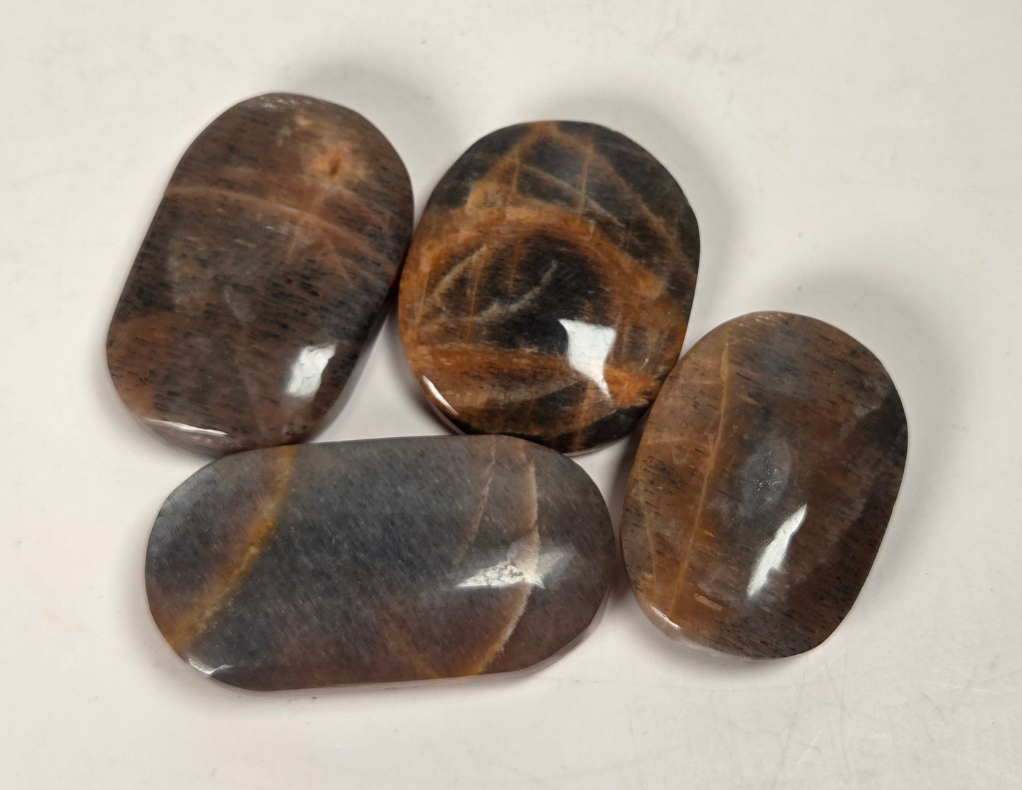 Four polished brown gemstone tumbled pendants with natural stone patterns, arranged on a light off-white background.