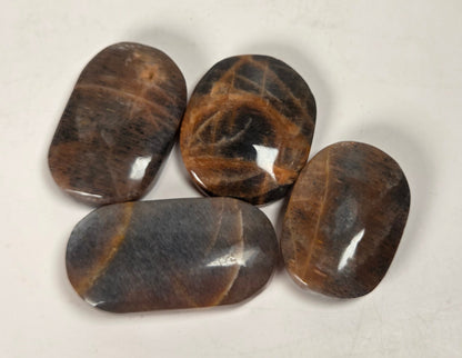 Four polished brown gemstone tumbled pendants with natural stone patterns, arranged on a light off-white background.