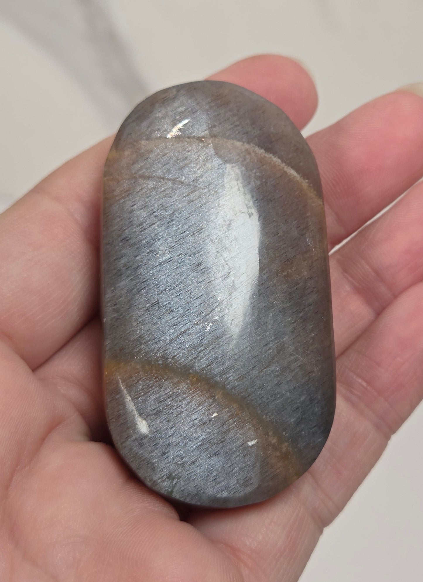 A hand holding a polished gray stone with subtle brown veining, set against a light marble-patterned background.