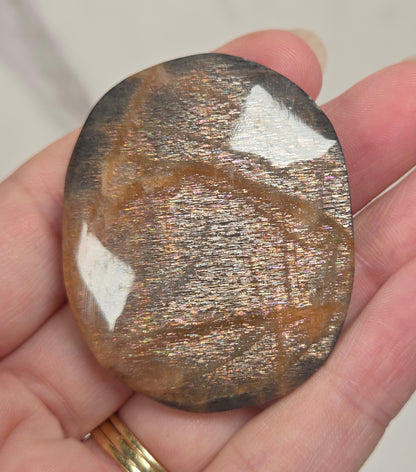 A polished cat's eye gemstone with a metallic, shimmering brown and gold surface, held in a person's hand.