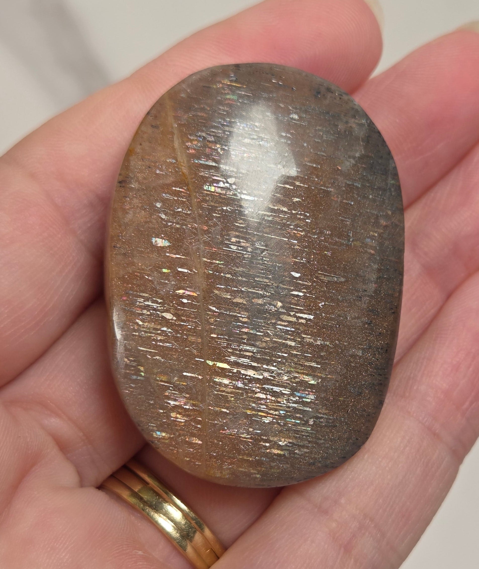 A polished brown stone with fine metallic-looking striations, held in a person's hand against a light marble-like background.