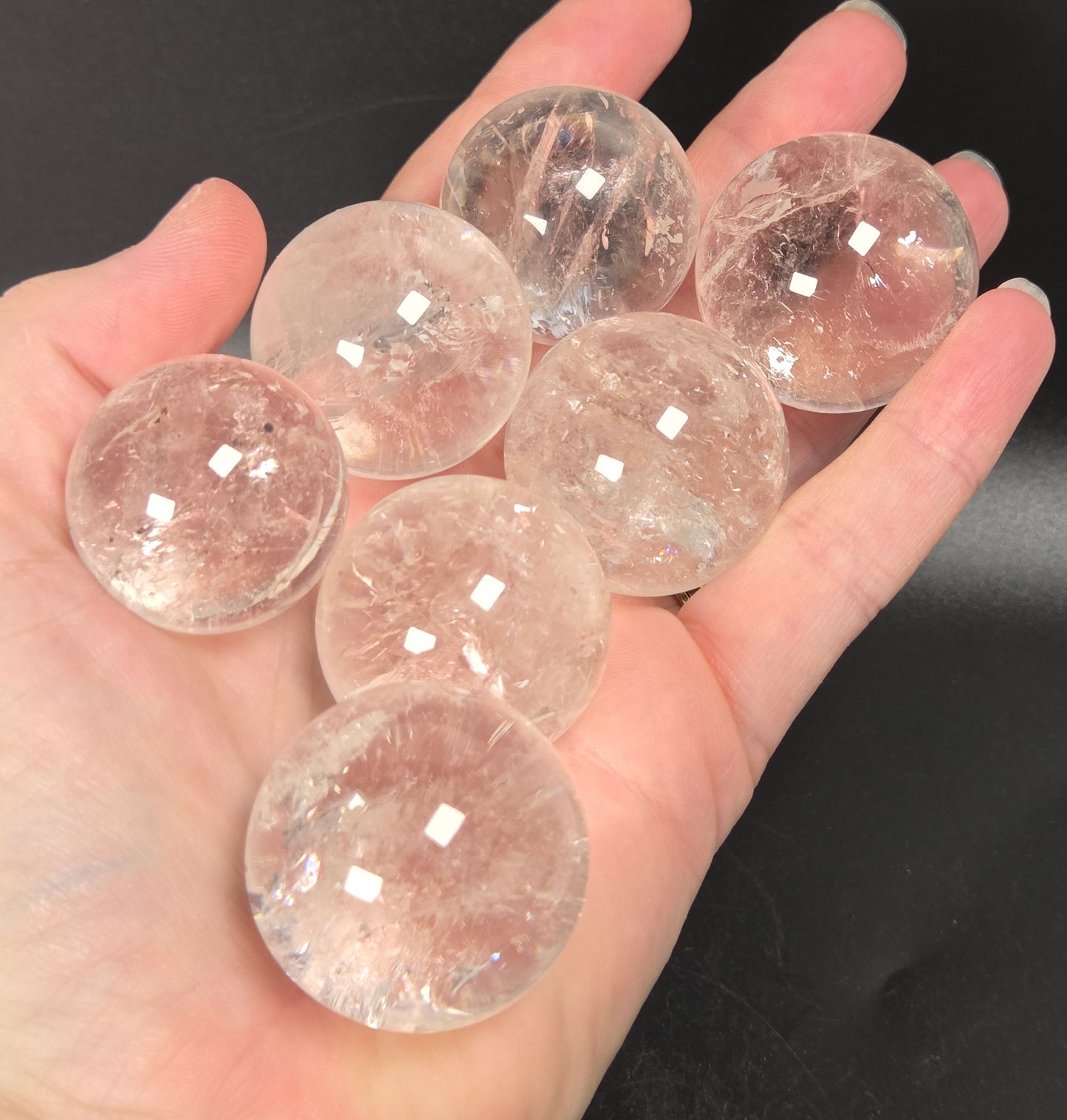 A hand holding seven clear, faceted crystal spheres with natural inclusions, set against a dark, solid background.