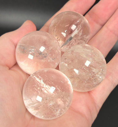 Four round, transparent clear quartz crystal balls resting on an open hand against a dark background.