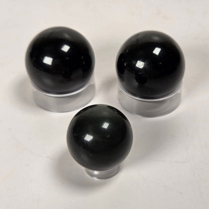 Three glossy black spherical objects displayed on clear stands against a plain light background.