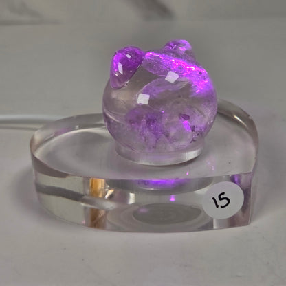 A small purple crystal cluster sculpture displayed on a clear acrylic stand with a white sticker marked '15' on it, set against a plain light gray background.