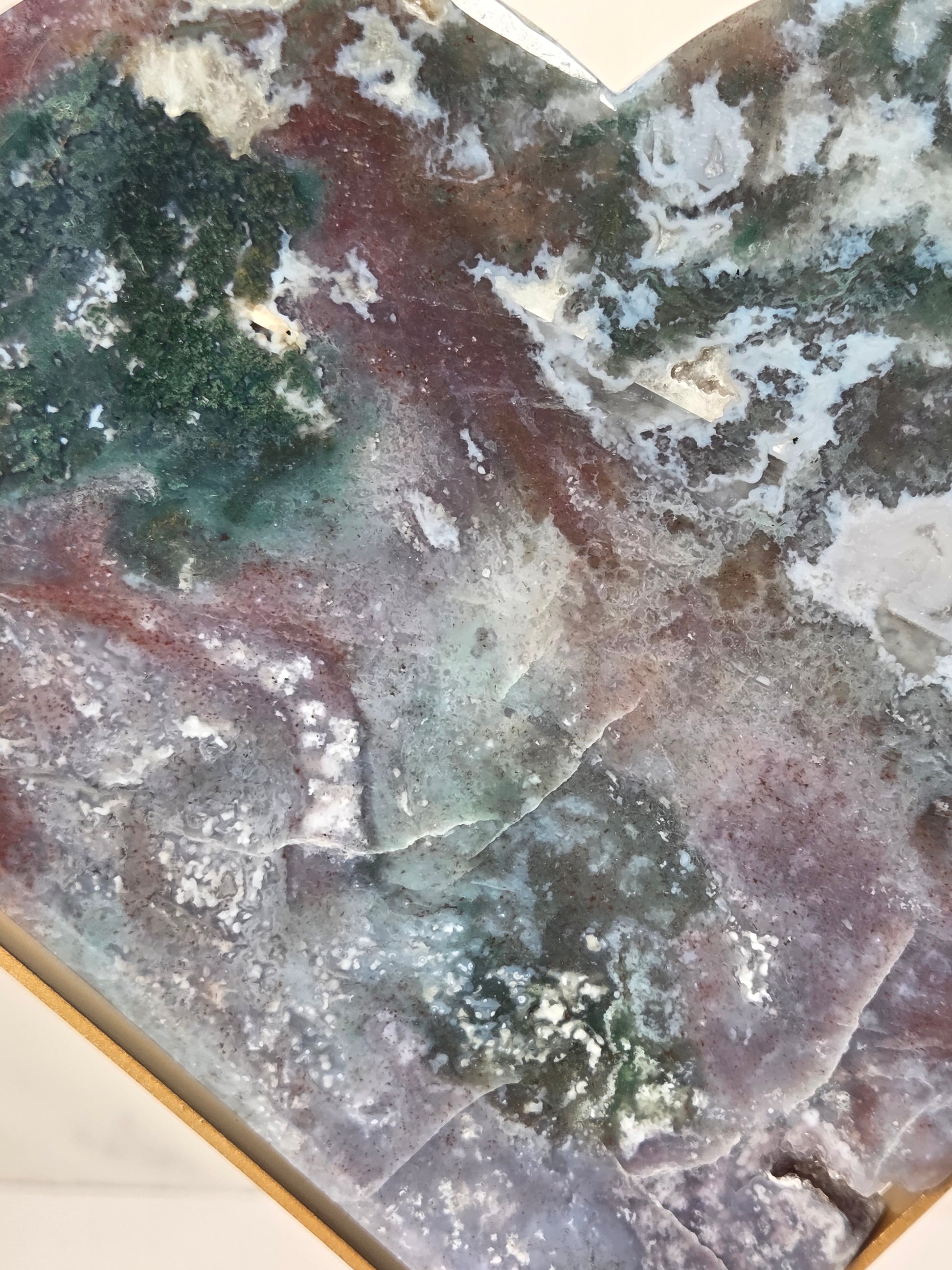 A close-up of a polished stone or mineral slab with marbled patterns in green, gray, purple, and reddish-brown, filling most of the frame.