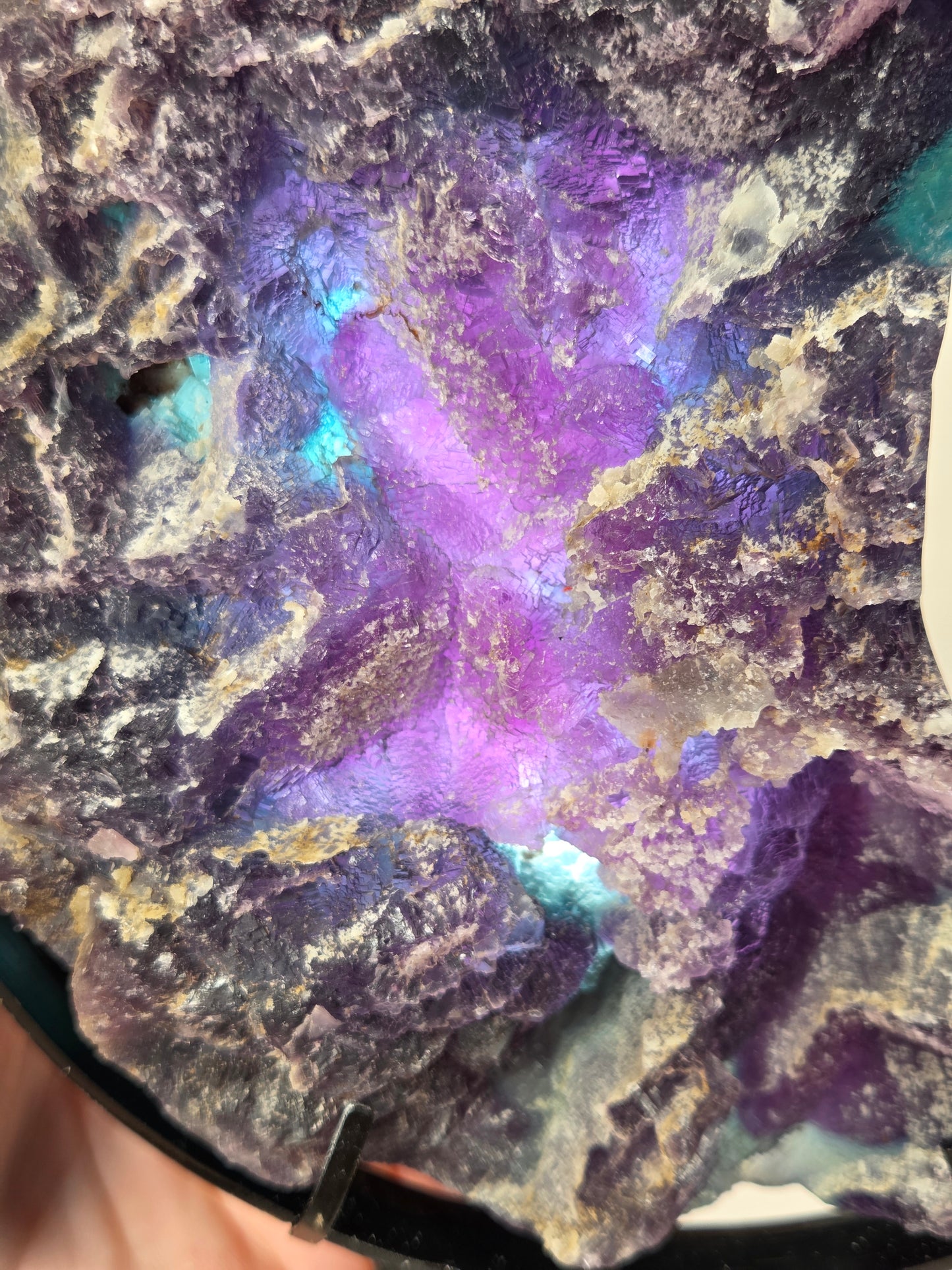 A close-up of a natural iridescent mineral specimen with a prominent purple and blue luster, showing textured crystalline formations and metallic-looking surface variations.