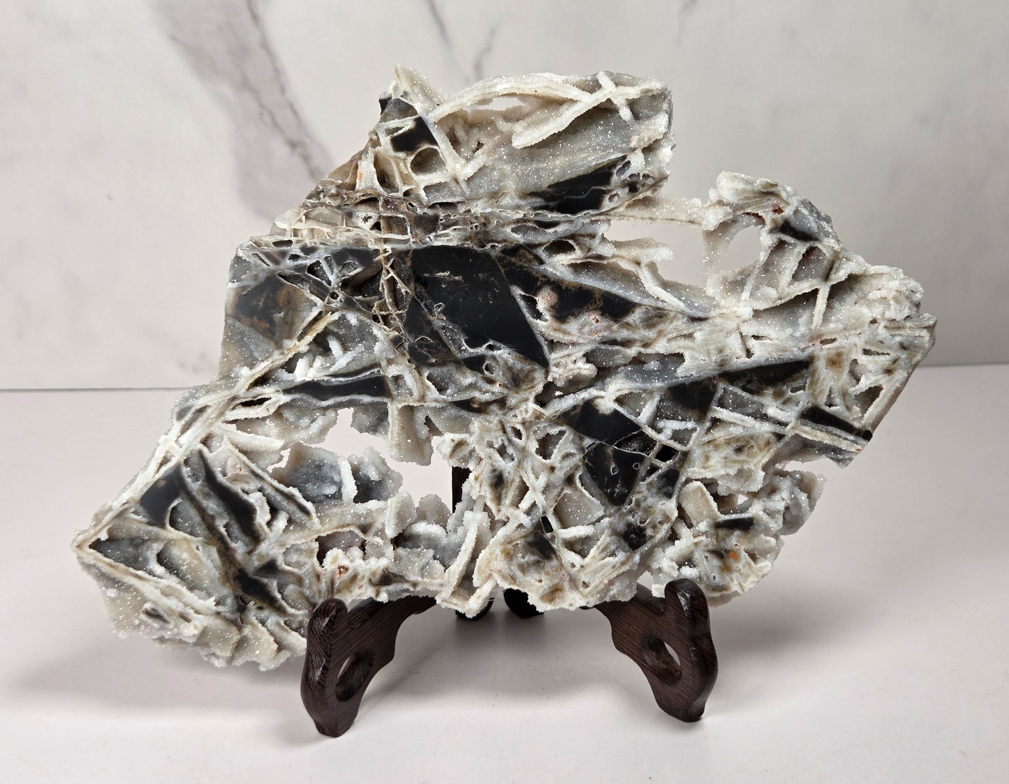 A polished black and white marble decorative rock sculpture with natural fissures, displayed on a small dark wooden stand against a light gray marble-patterned background.