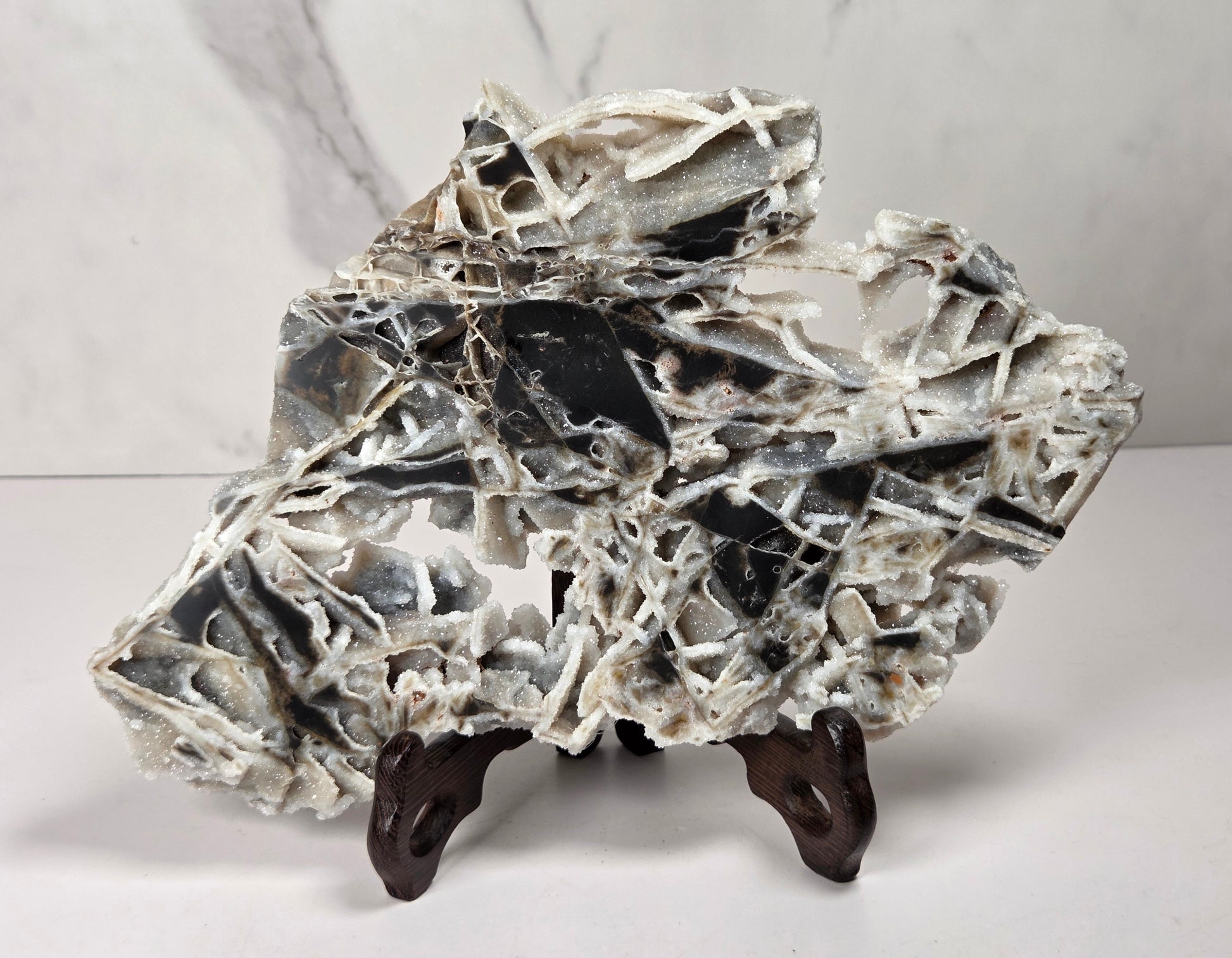 A polished black and white marble decorative rock sculpture with natural fissures, displayed on a small dark wooden stand against a light gray marble-patterned background.