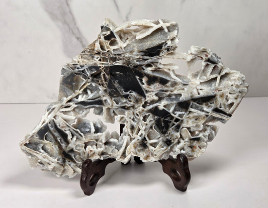 A polished black and white marble decorative rock sculpture with natural fissures, displayed on a small dark wooden stand against a light gray marble-patterned background.