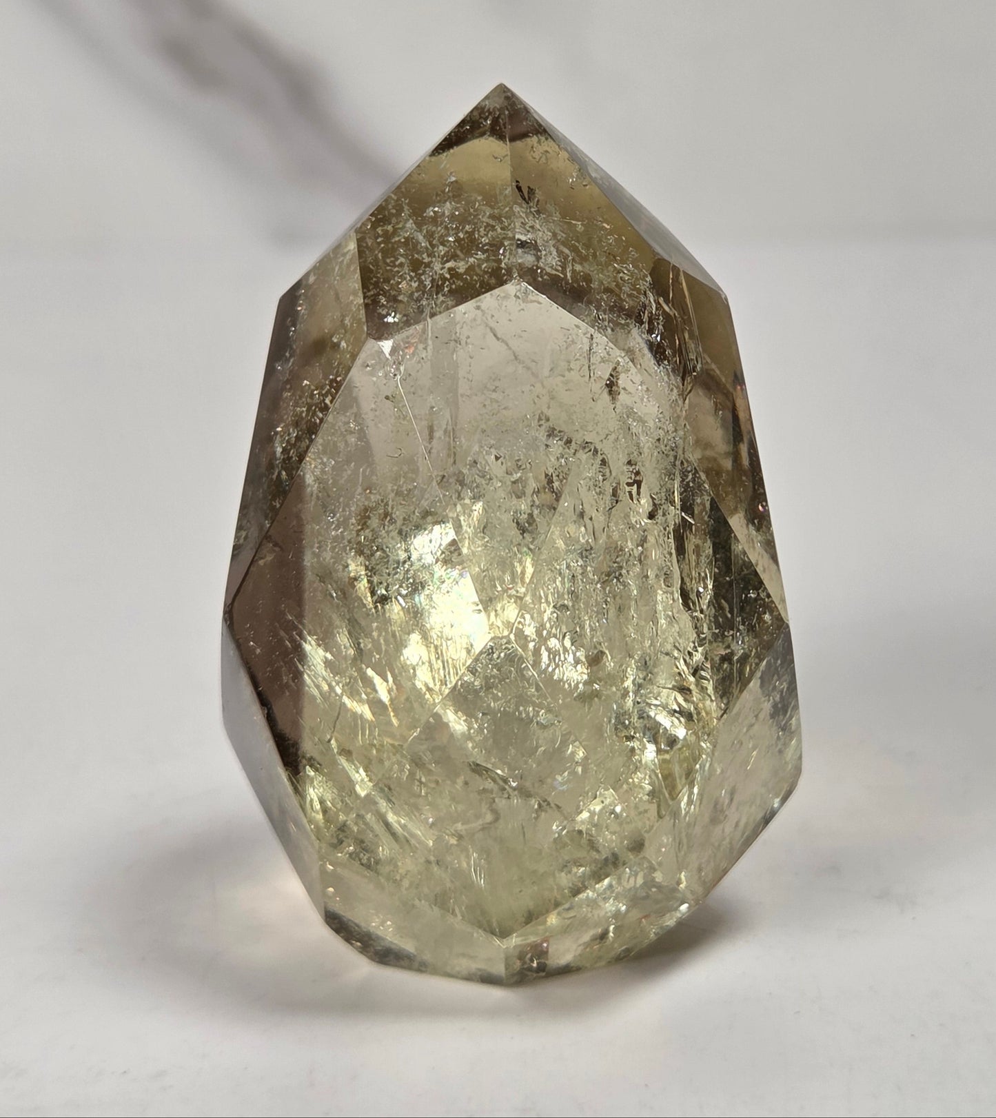 A faceted natural crystal gemstone with a pointed top, showing internal inclusions and a warm gray-brown translucent tone, photographed on a plain light background.
