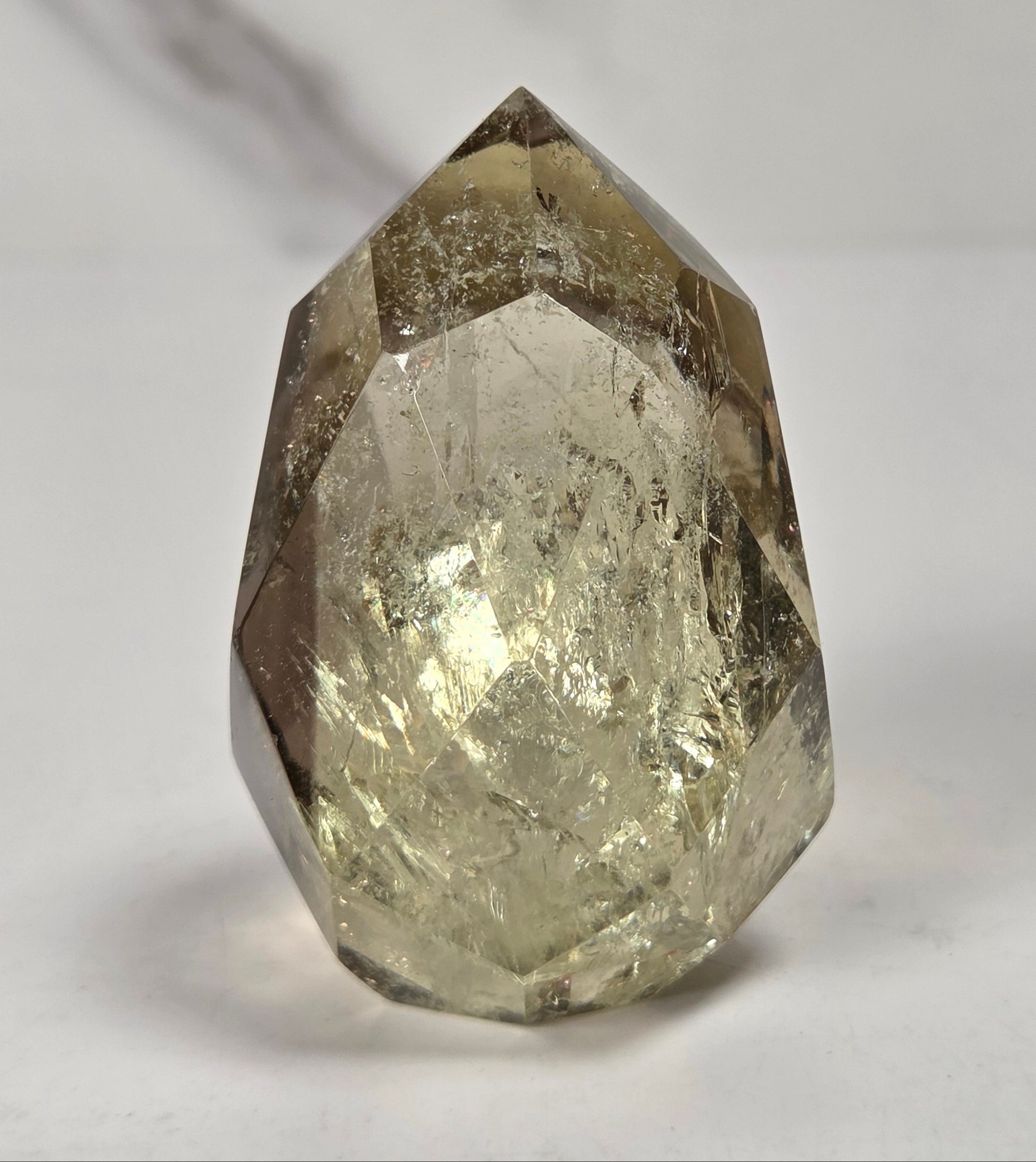 A faceted natural crystal gemstone with a pointed top, showing internal inclusions and a warm gray-brown translucent tone, photographed on a plain light background.