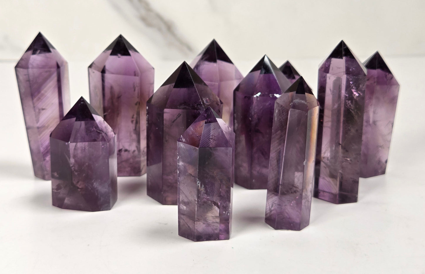 A group of natural amethyst crystal points of various heights arranged on a white surface with a light gray marble background.