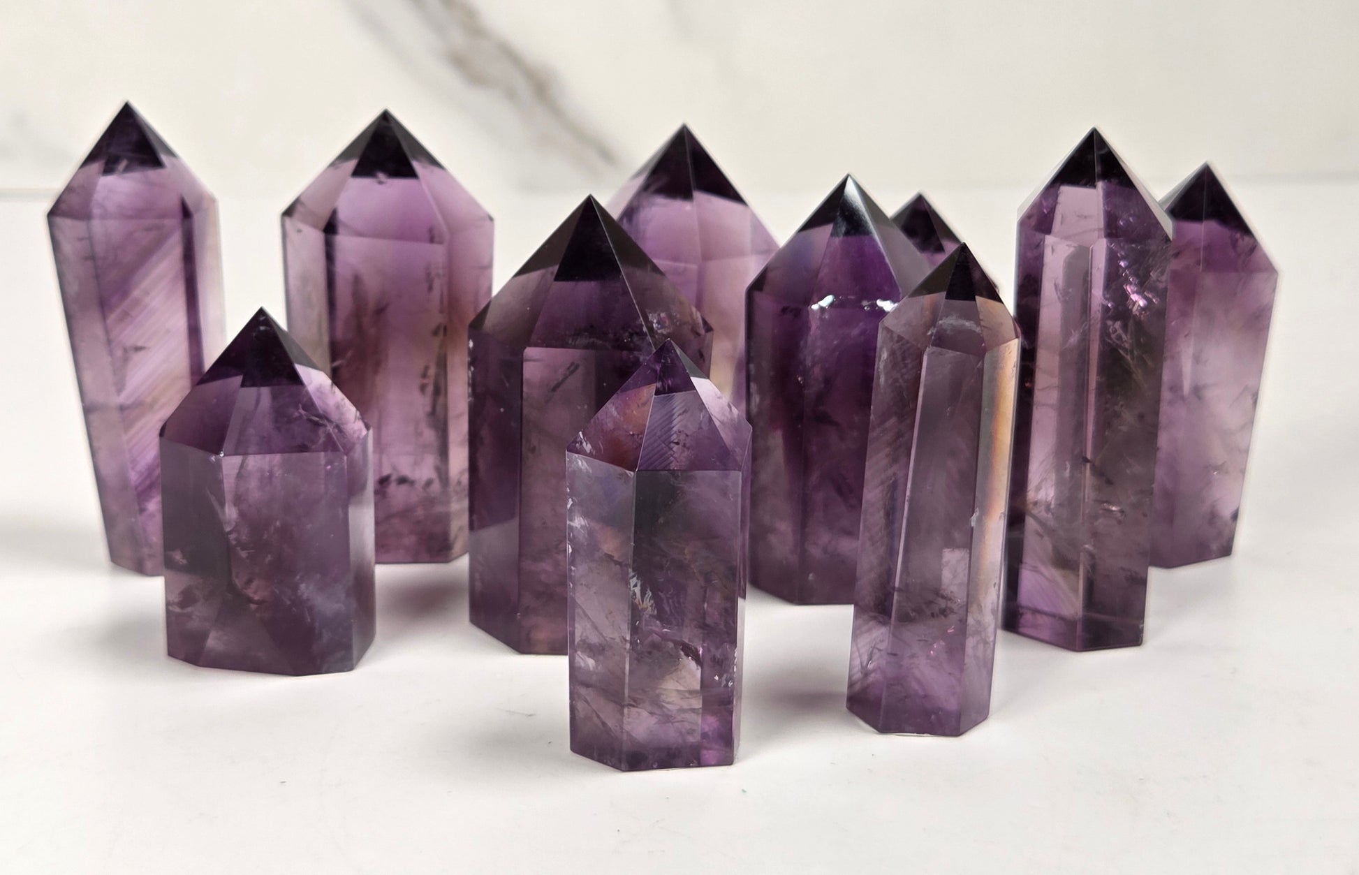 A group of natural amethyst crystal points of various heights arranged on a white surface with a light gray marble background.