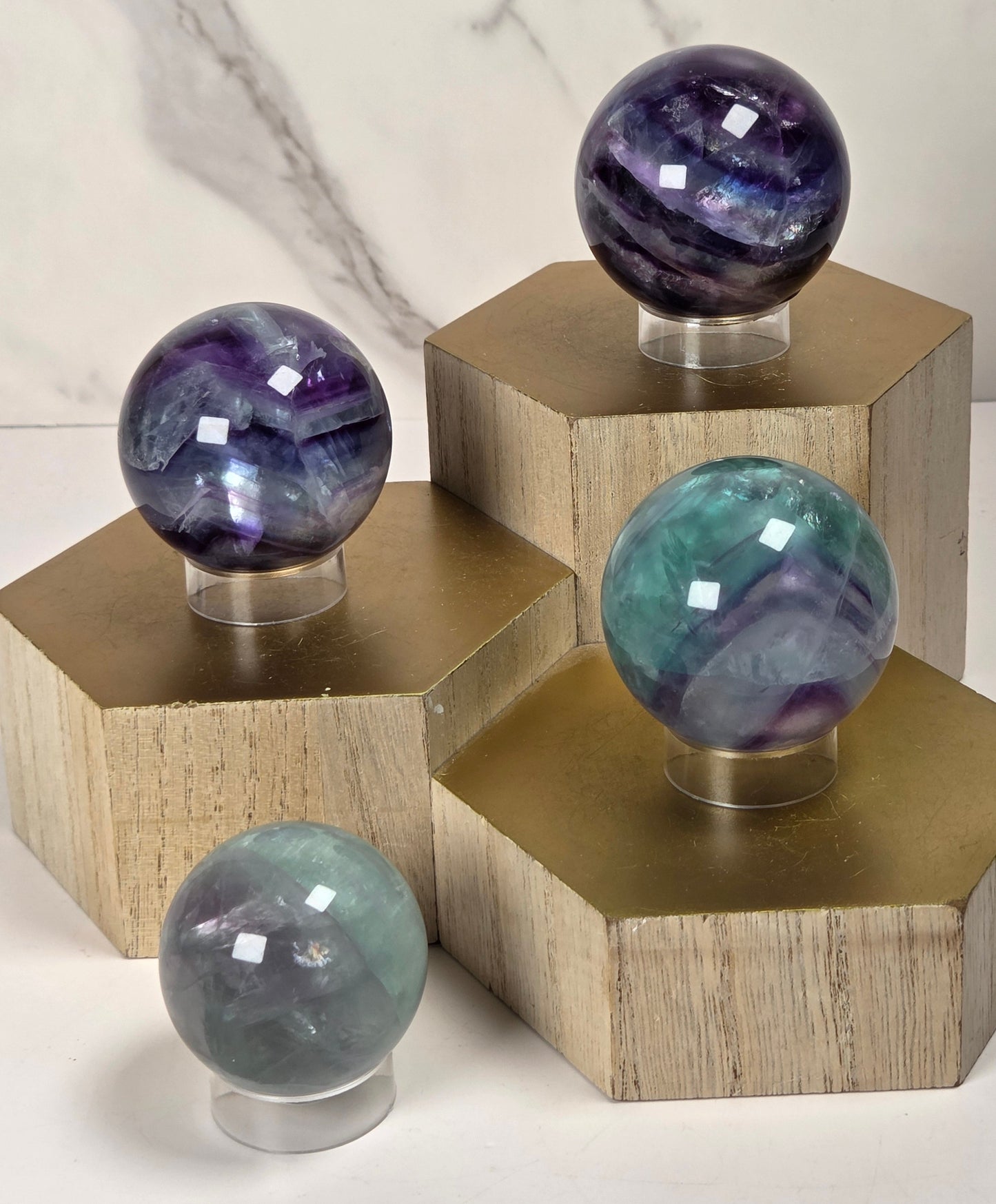 Collection of polished multi-colored fluorite crystal sphere on a clear acrylic stand, displayed on a gold-colored block.