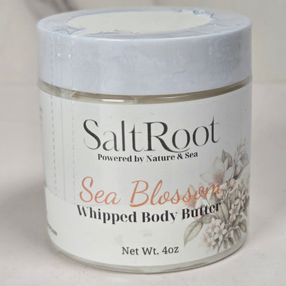 A jar of SaltRoot Sea Blossom Whipped Body Butter on a light, neutral background. The product is in a clear glass jar with a white lid and a white label featuring black and coral text.