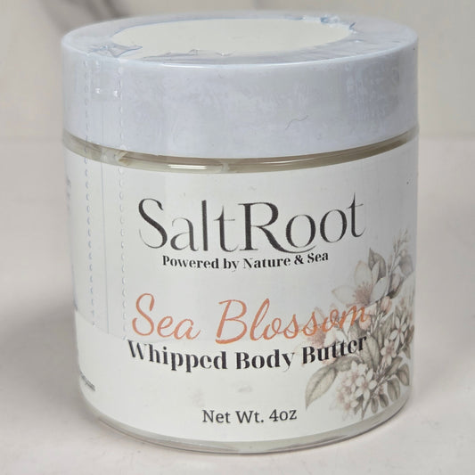 A jar of SaltRoot Sea Blossom Whipped Body Butter on a light, neutral background. The product is in a clear glass jar with a white lid and a white label featuring black and coral text.