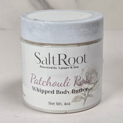 A jar of SaltRoot Patchouli Rose Whipped Body Butter on a light marble-like surface with a soft gray background.