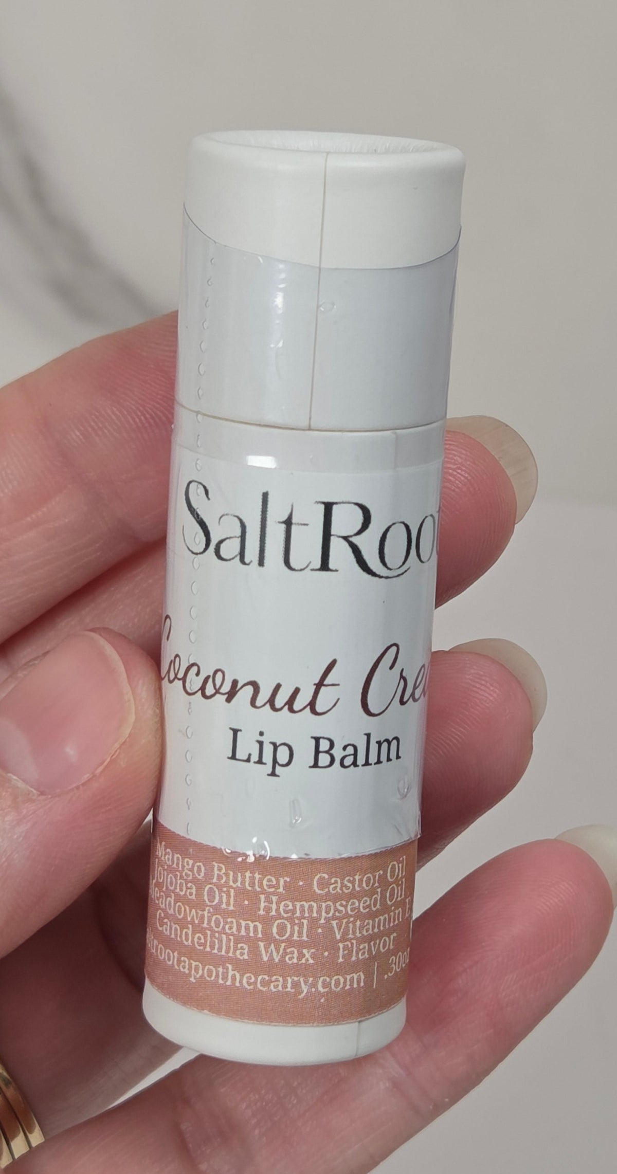 Hand holding a tube of coconut cream lip balm against a white background
