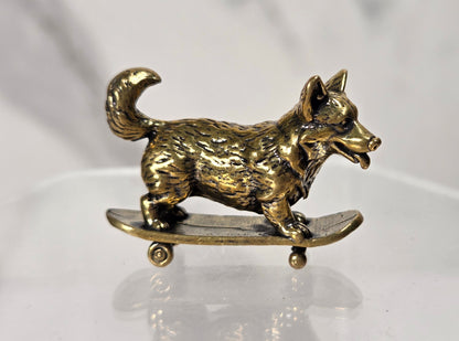 A small metallic dog figurine standing on a miniature skateboard, photographed on a clear acrylic display stand against a soft light gray background.