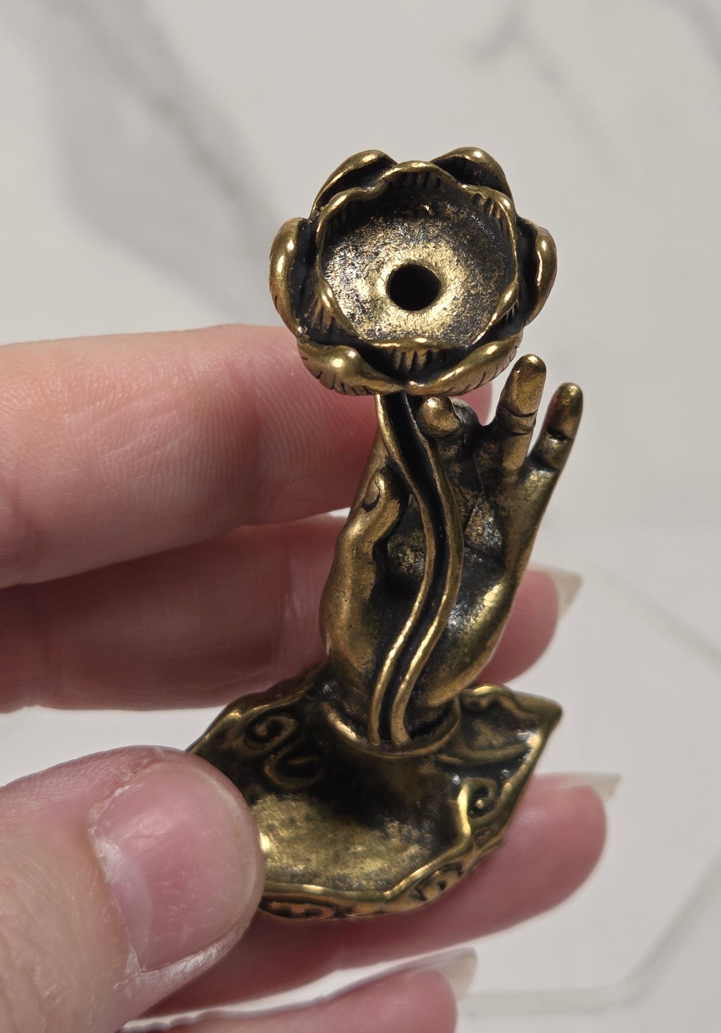 A small antique-style brass figurine of a lotus flower held in a person's hand against a light marble-patterned background.