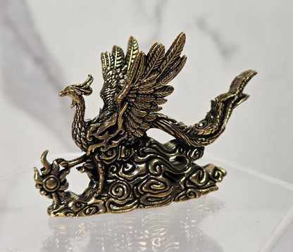 An antique bronze phoenix figurine standing on stylized clouds, displayed on a clear acrylic stand against a light gray marble-patterned background.