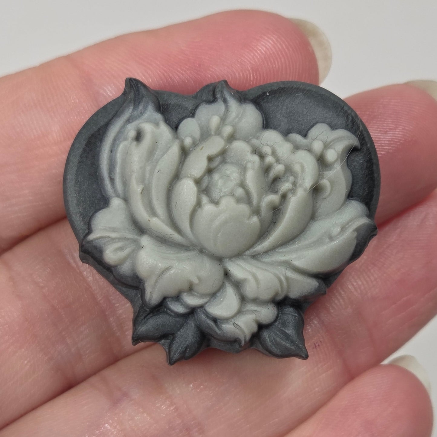 A heart-shaped dark gray wax seal with a carved white and gray lotus flower, held in a person's hand.