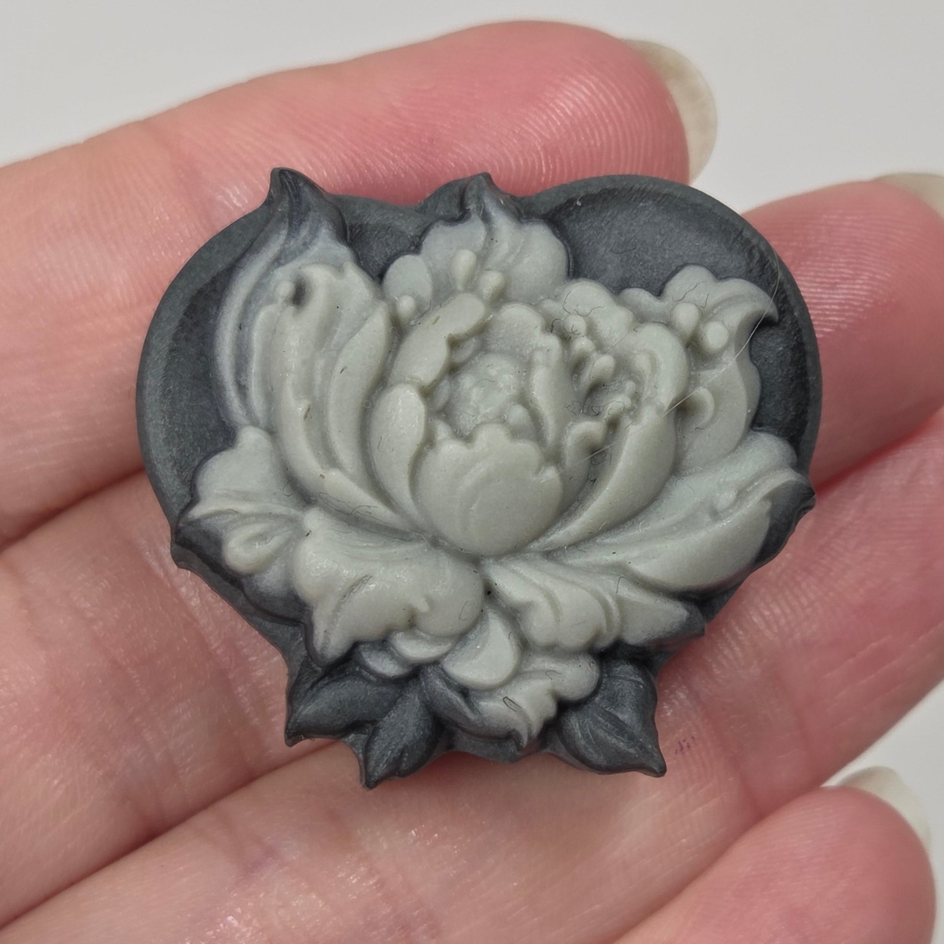 A heart-shaped dark gray wax seal with a carved white and gray lotus flower, held in a person's hand.