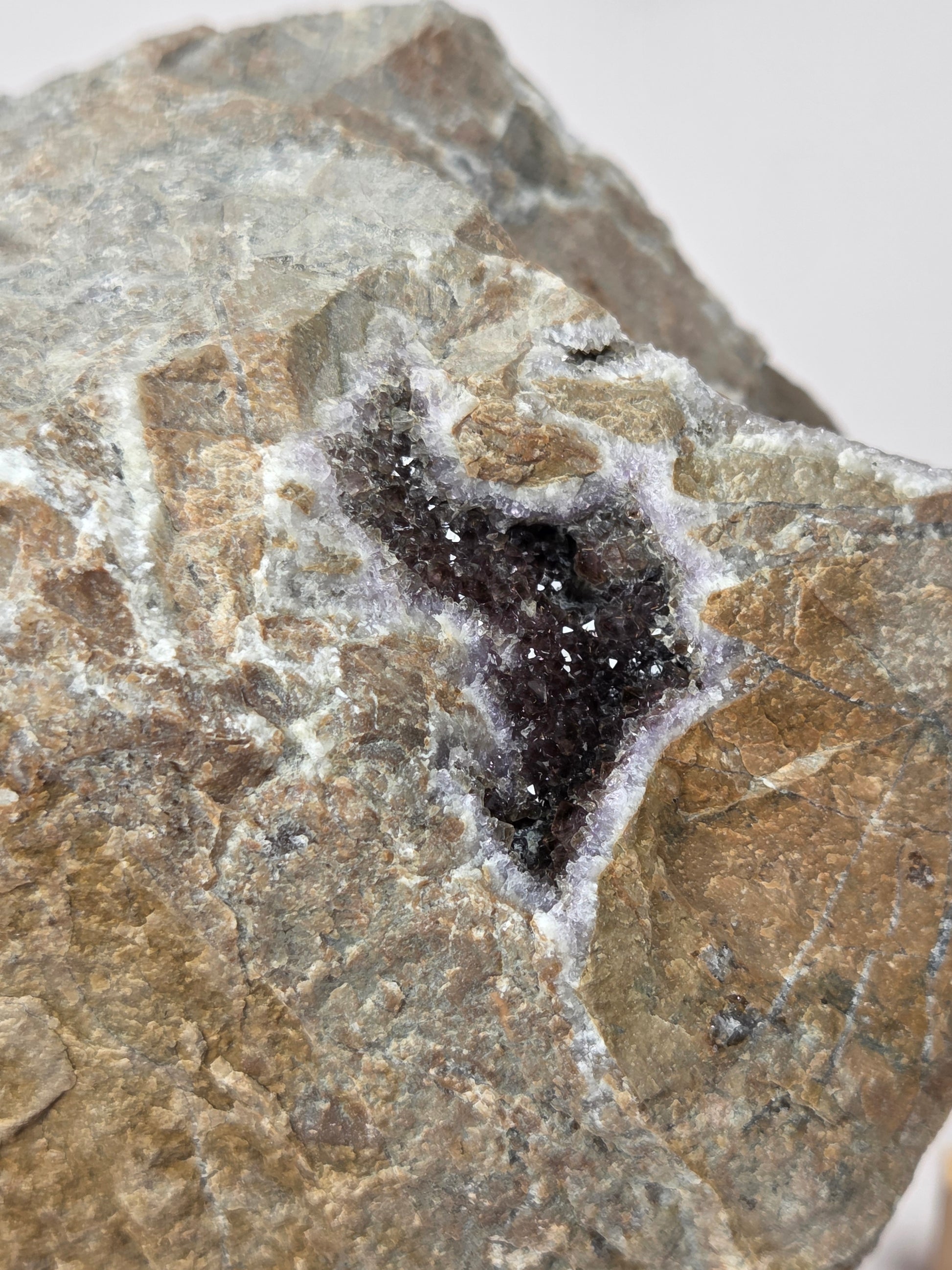 A close-up of a natural rock specimen with a dark, almost black geode cavity surrounded by white crystalline mineral growth and a tan-brown outer rock matrix.
