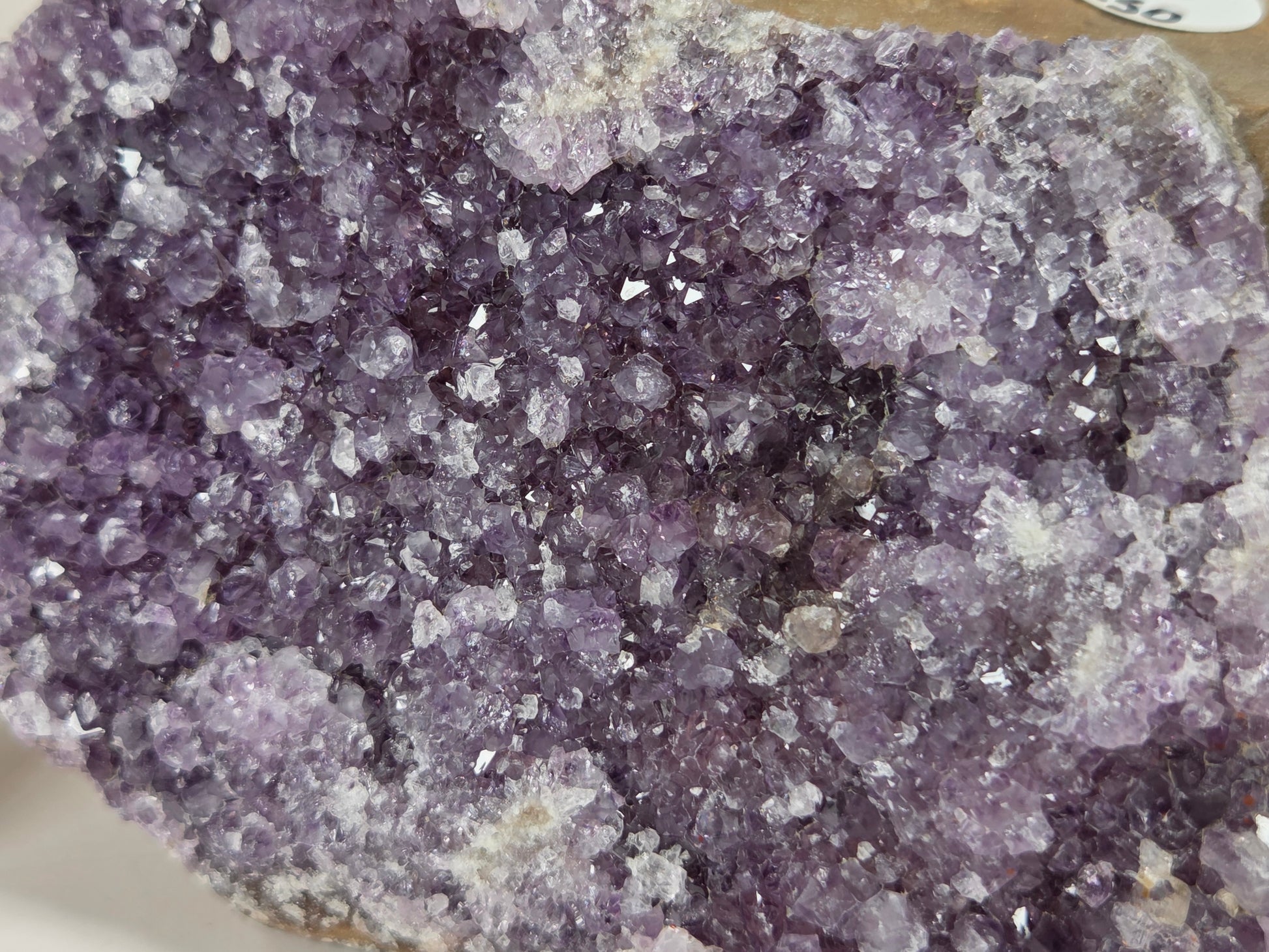 A close-up of an amethyst crystal cluster or geode specimen with dense purple and lavender crystalline structure and some lighter translucent areas.