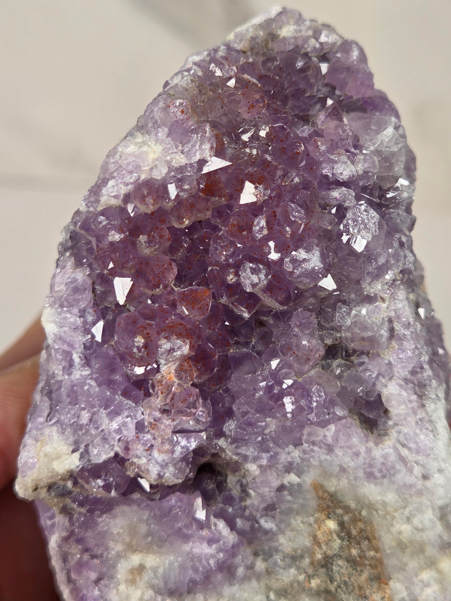 A close-up of a purple amethyst crystal cluster specimen being held, showing faceted translucent crystals on a light stone matrix.